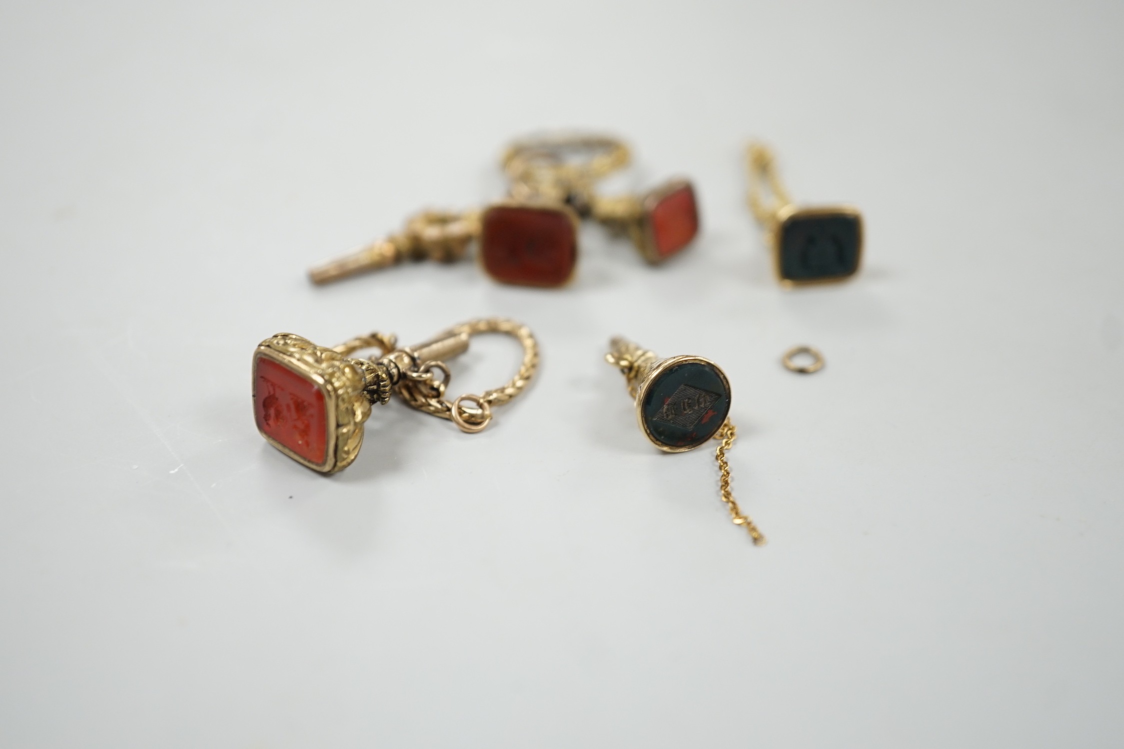 Two 19th century yellow metal overlaid and bloodstone set watch key fobs, one of funnel form, 21mm, a similar gold plated and carnelian set watch key fob, two other fob seals and a watch key on chain.